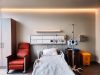 Pfizer Drug Ponsegromab Boosts Weight in Cachexia Trial A cancer patient in a hospital bed holds a plate of food while a doctor reviews a chart showing weight gain data from a ponsegromab trial.