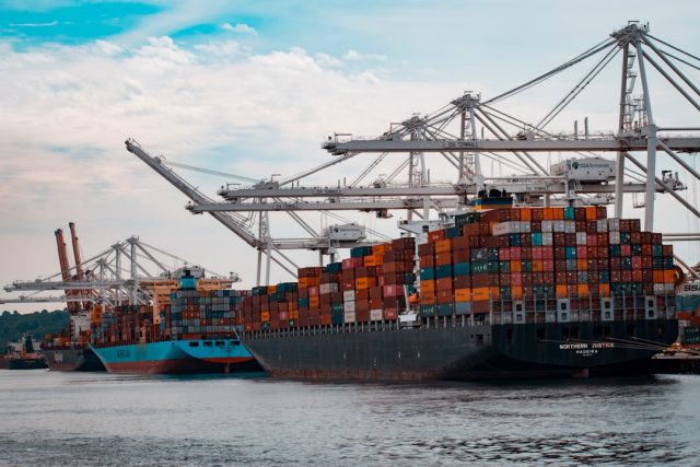 Chemical Spill From Capsized Tanker Off Japan Kills Eight, Two Missing A red-hulled chemical tanker lies capsized in grey seas while response vessels circle and a pale chemical sheen drifts downstream.