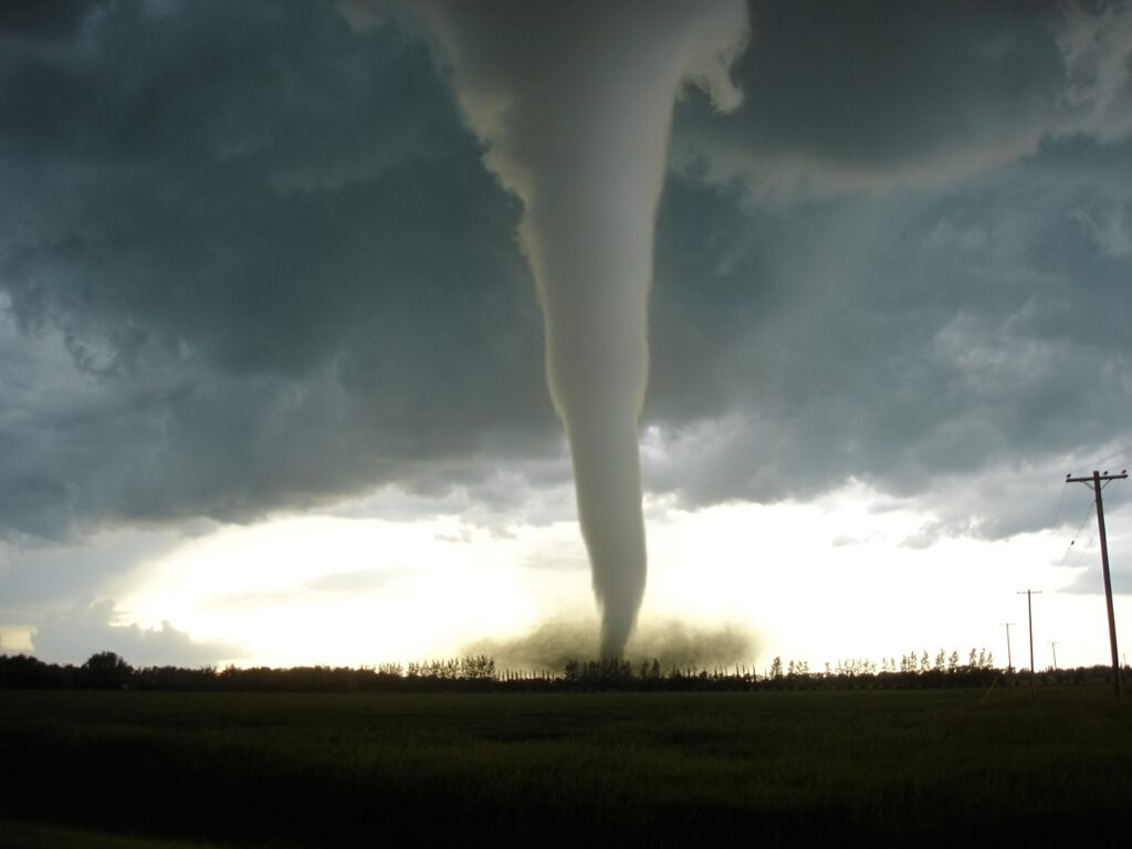A tornado funnel cloud touches down over a rural Indiana landscape with debris swirling near the ground.