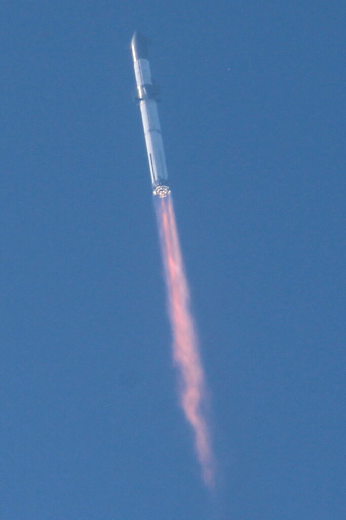 Starship lifts off from Boca Chica, Super Heavy engines blazing in a cloud of dust and fire.