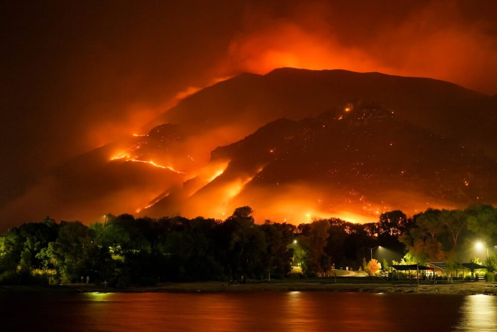 Aerial view of a wildfire burning through forest and hills near residential areas in British Columbia.