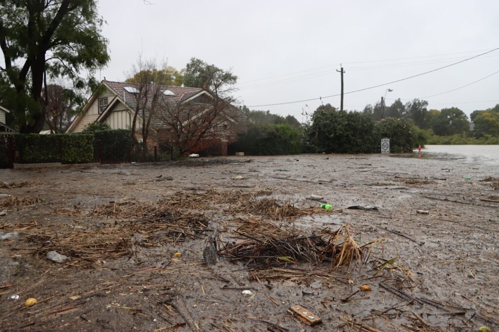 Floodwater surges through a muddy Eastern Cape settlement, washing away makeshift homes and leaving debris along cracked roads.